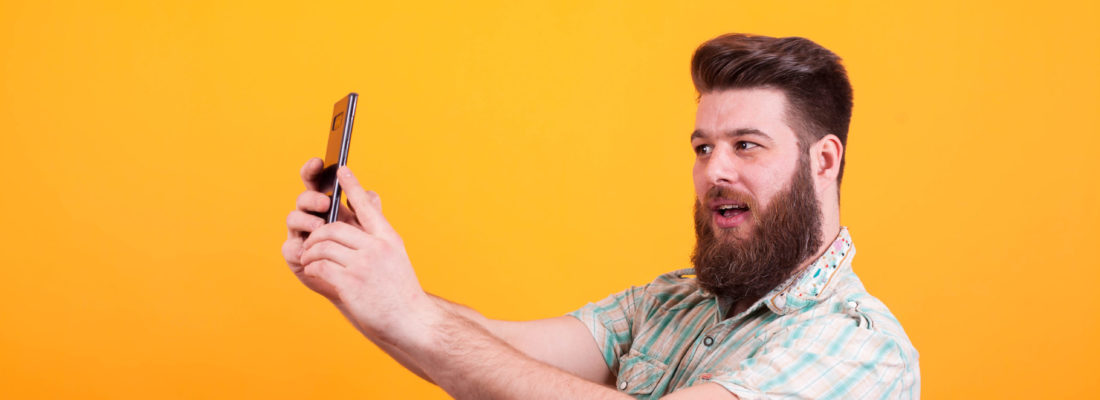 Hipster bearded man having a video call on his phone over yellow background Hipster bearded man having a video call on his phone over yellow background. Expressive man.