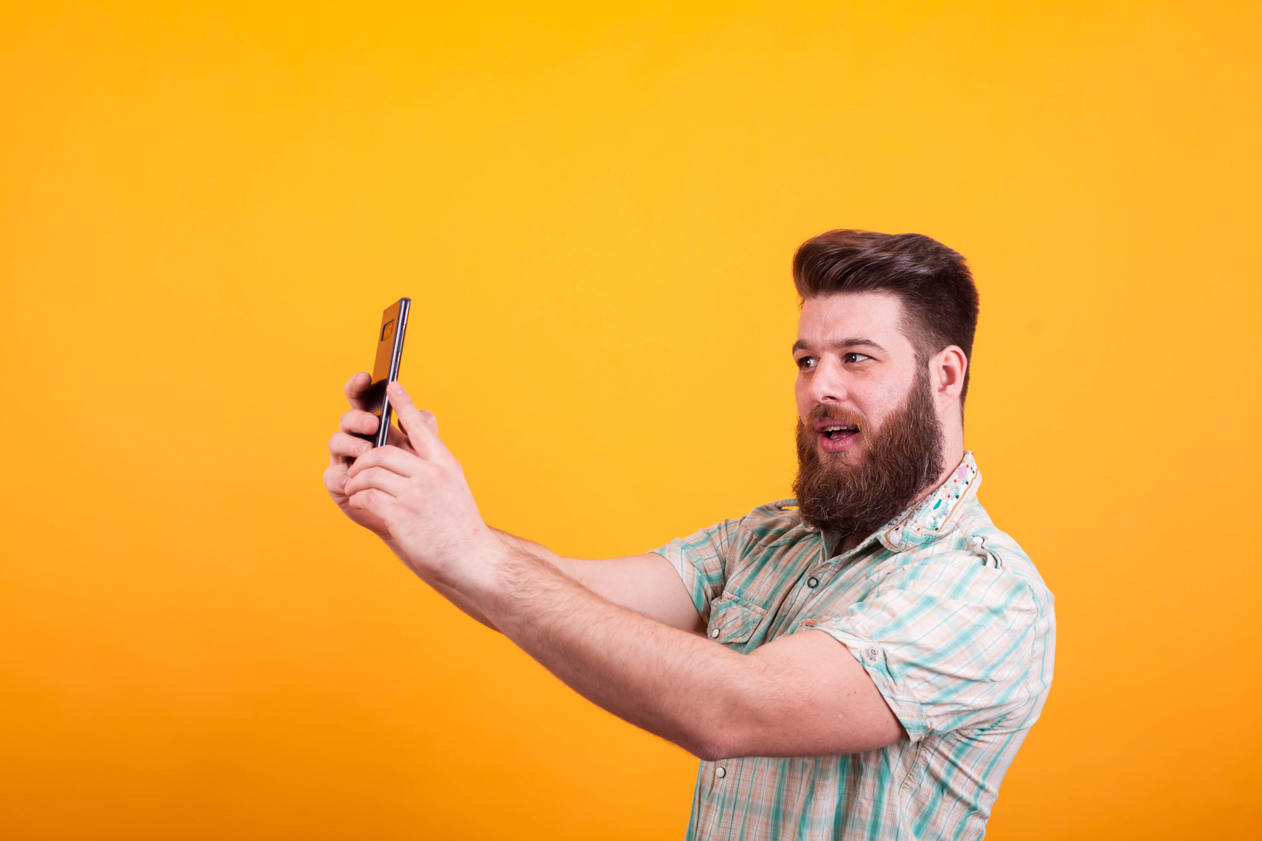 Hipster bearded man having a video call on his phone over yellow background